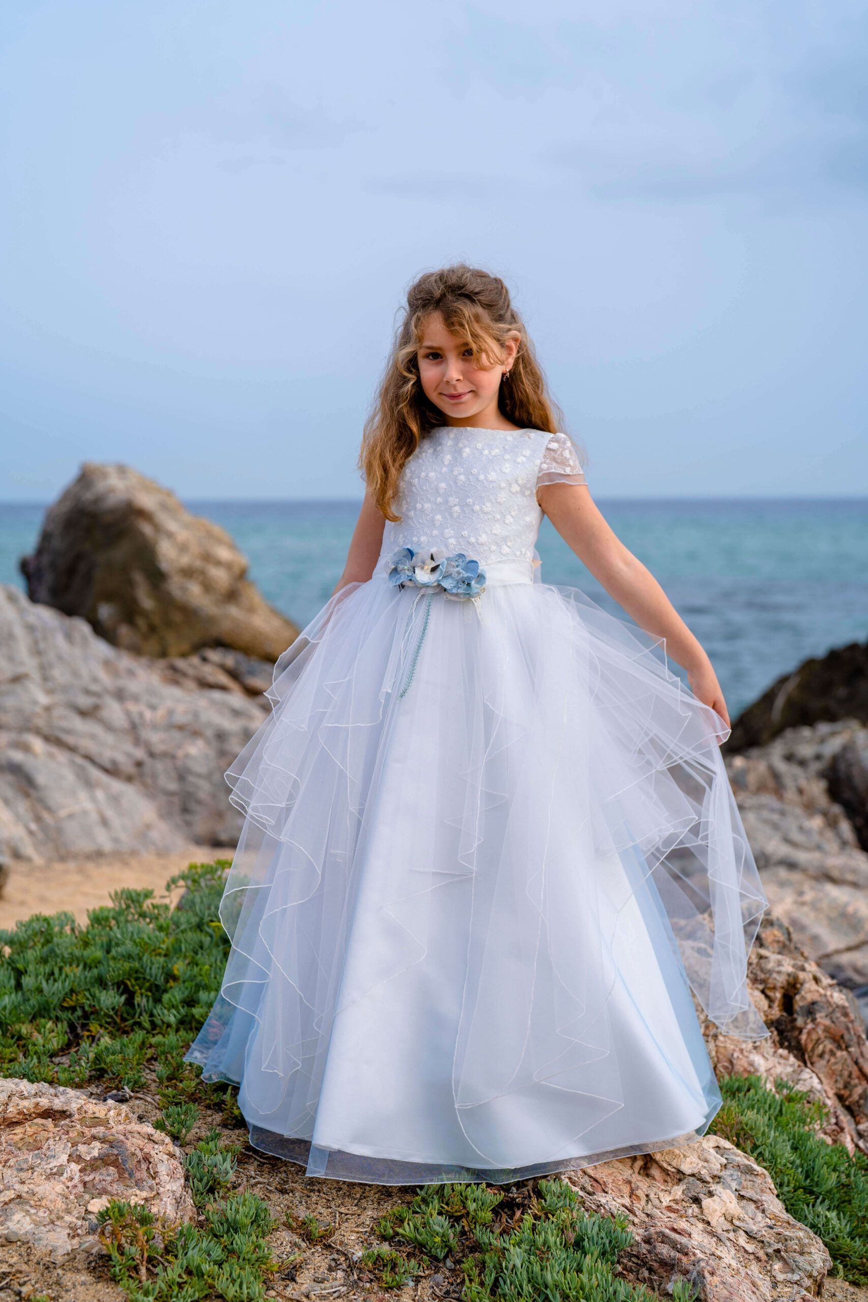 vestido de comunión Co & Ce en tul celeste con cuerpo bordado y flores en la cintura