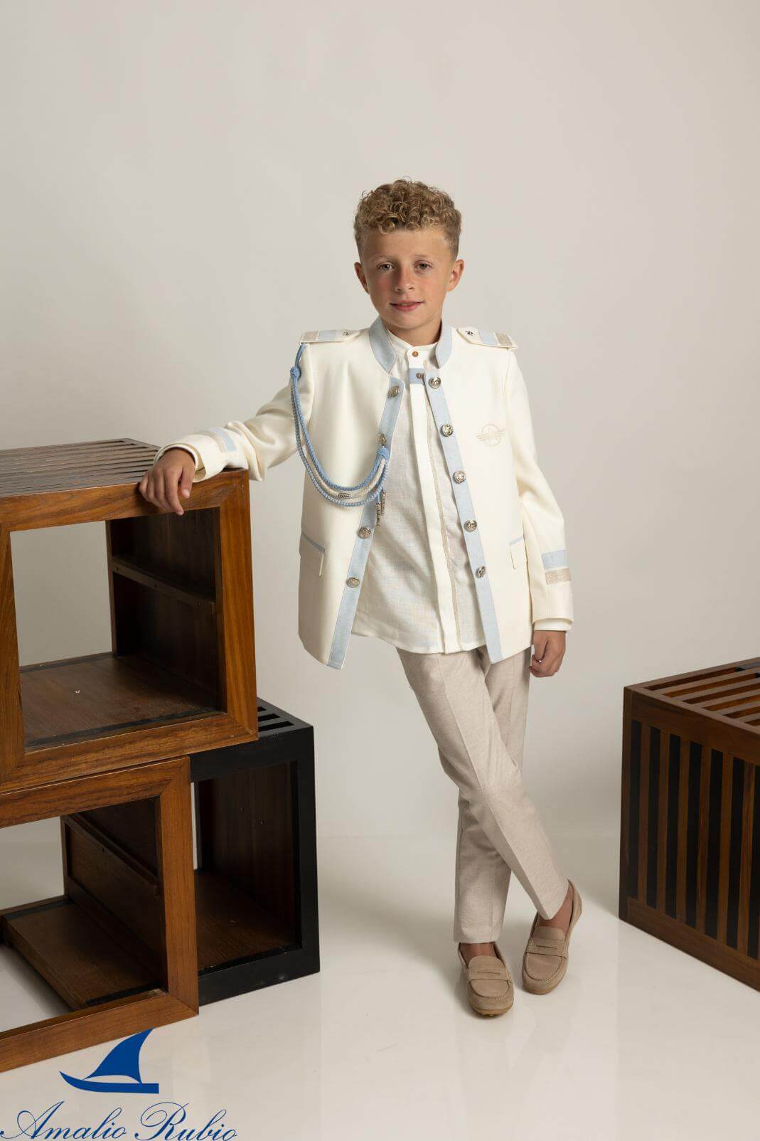 Traje de Comunión almirante Amalio Rubio con chaqueta beige de cuello Mao, adornos celestes, camisa con vivos en la abotonadura y pantalón celeste.