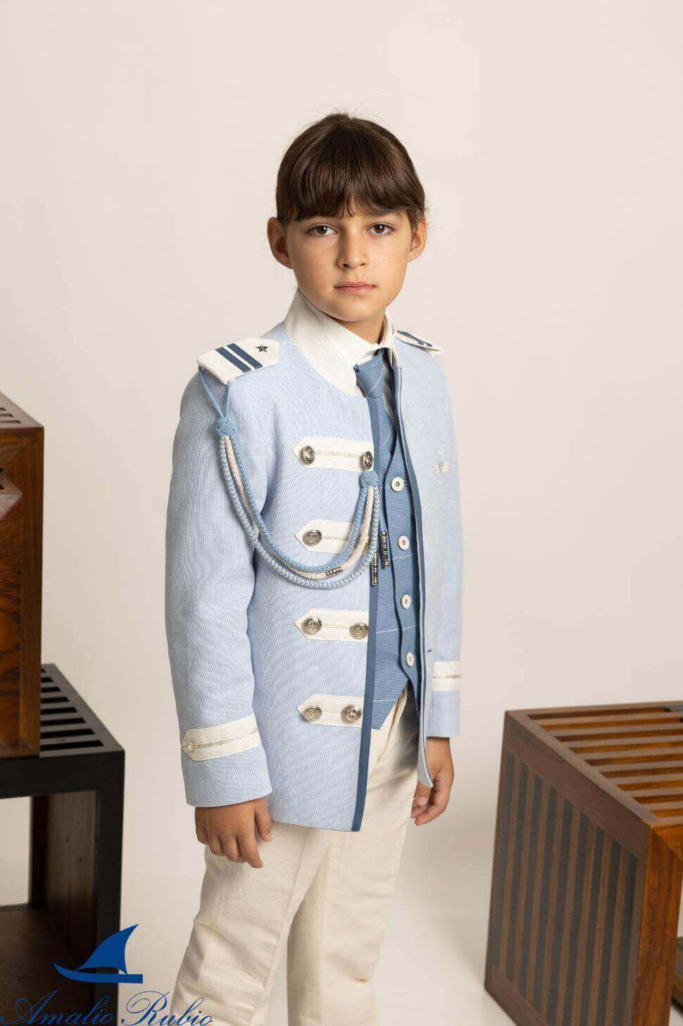 Traje de Comunión almirante Amalio Rubio con chaqueta celeste, pasamanería beige y azul, camisa de cuello camisero, corbata a juego y pantalón beige.